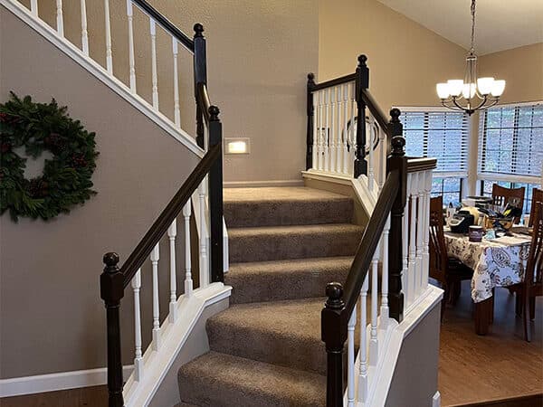 Carpeted staircase beside beige walls, white balusters, and dark wood handrails.