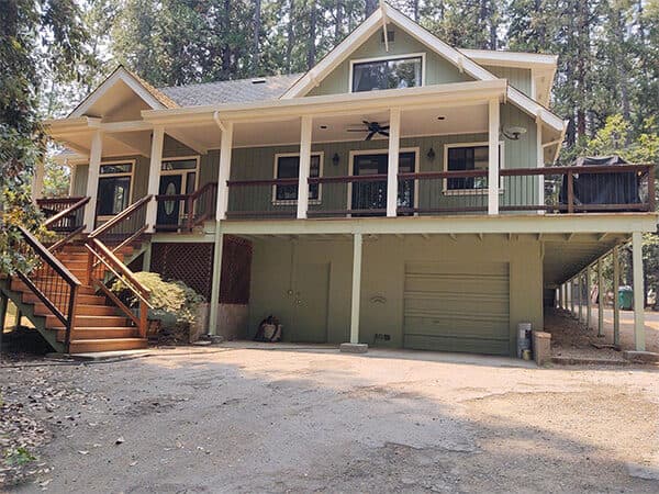 Green house exterior with cream trim, a covered porch, and wood entry stairs.