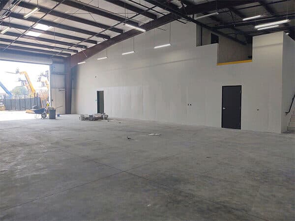 Warehouse interior with light-colored walls, exposed roof framing, and a concrete floor.