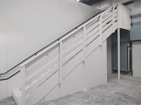 Interior staircase with white railings and dark handrails beside a light-colored wall.