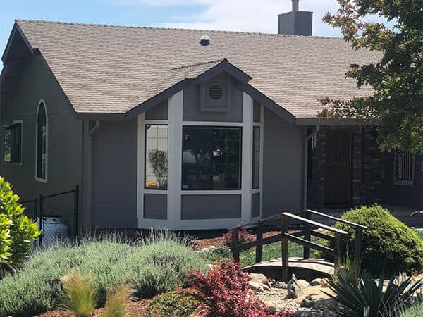 Gray house exterior with white trim around a projecting window and a wood footbridge.