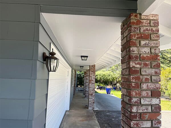 Covered porch with gray horizontal siding, a white ceiling, and brick columns.